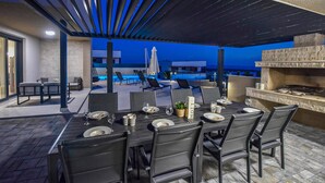 Un área de comedor exterior con vista a la piscina, una parrilla y un diseño moderno.