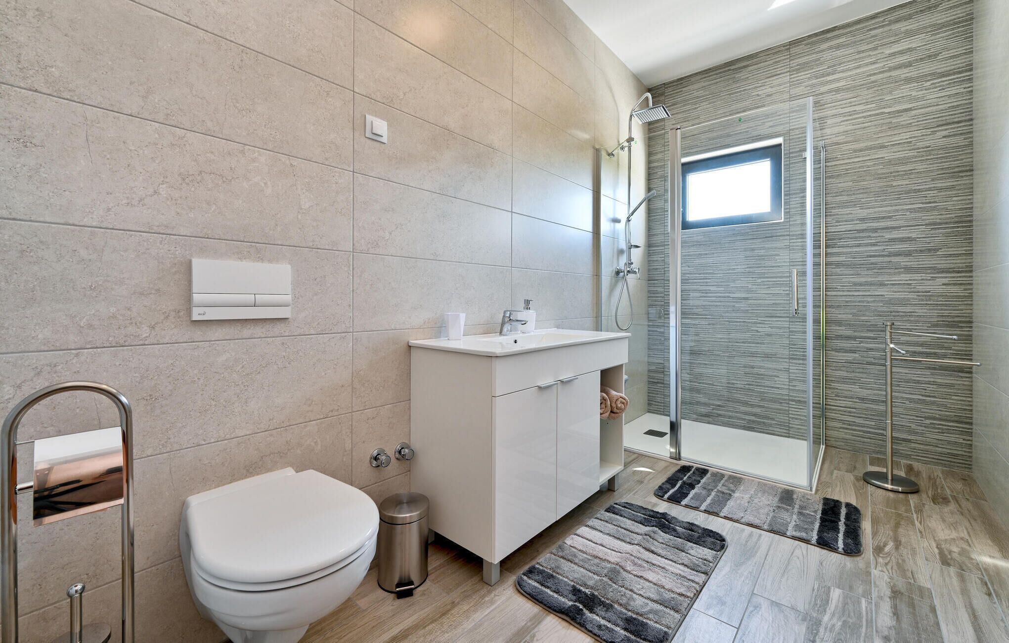 Et moderne badeværelse med toilet, vask, brusebad og et lille vindue.