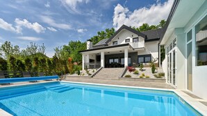 Una casa moderna con piscina, terraza cubierta y jardín ajardinado.