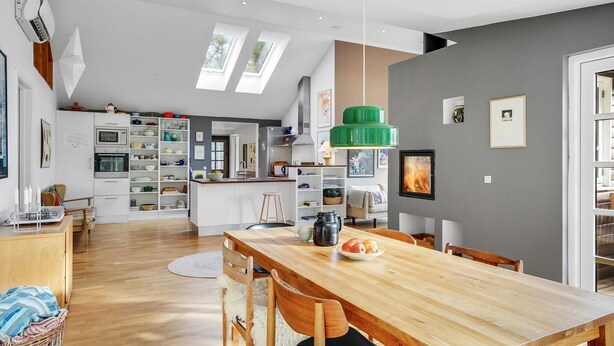 A modern kitchen with a central island, a dining area with a wooden table, and a grey accent wall. - Cozy home in Grenaa with WiFi (Grenaa)