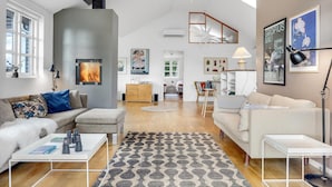 A modern living room with a grey accent wall, a fireplace, and a view of the garden. - Cozy home in Grenaa with WiFi (Grenaa)