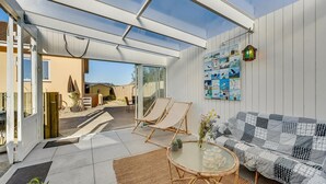 A spacious patio with a glass ceiling, a wicker sofa, a round glass table, and a wall with nautical-themed artwork. - 3 bedroom nice home in Hvide Sande (Hvide Sande)