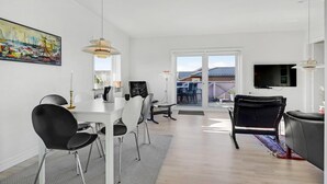 A modern living room with a dining area, a TV mounted on the wall, and a large window with a view of the outside. - 3 bedroom nice home in Hvide Sande (Hvide Sande)