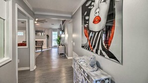 A hallway with a modern design, featuring a large abstract painting on the wall, a decorative console table, and a view into the dining area. - LUXURY GETAWAY, 4 BR, 2.5 BATH, NEAR FT. STEWART (Hinesville)