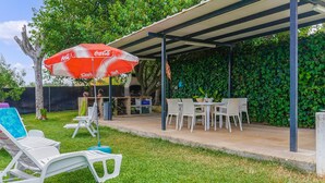An outdoor patio with a barbecue grill, white plastic chairs, and a red umbrella.