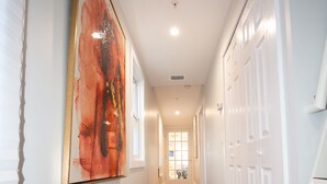 A hallway with wooden flooring, white walls, and a large abstract painting. - TROPICAL PROPERTIES VACATION RENTAL - KEY WEST (Key West)