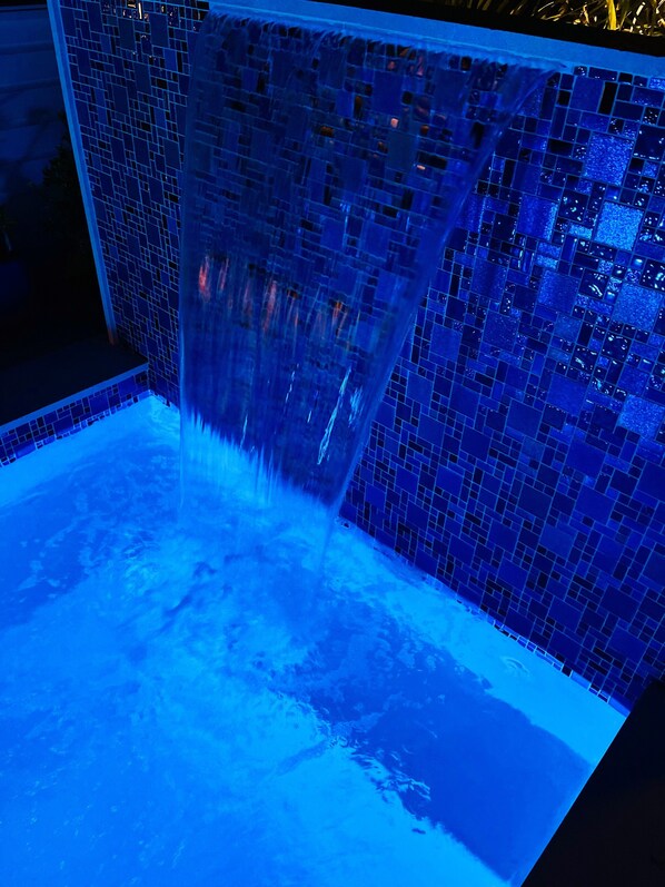 A blue-lit water feature with a mosaic tile wall.