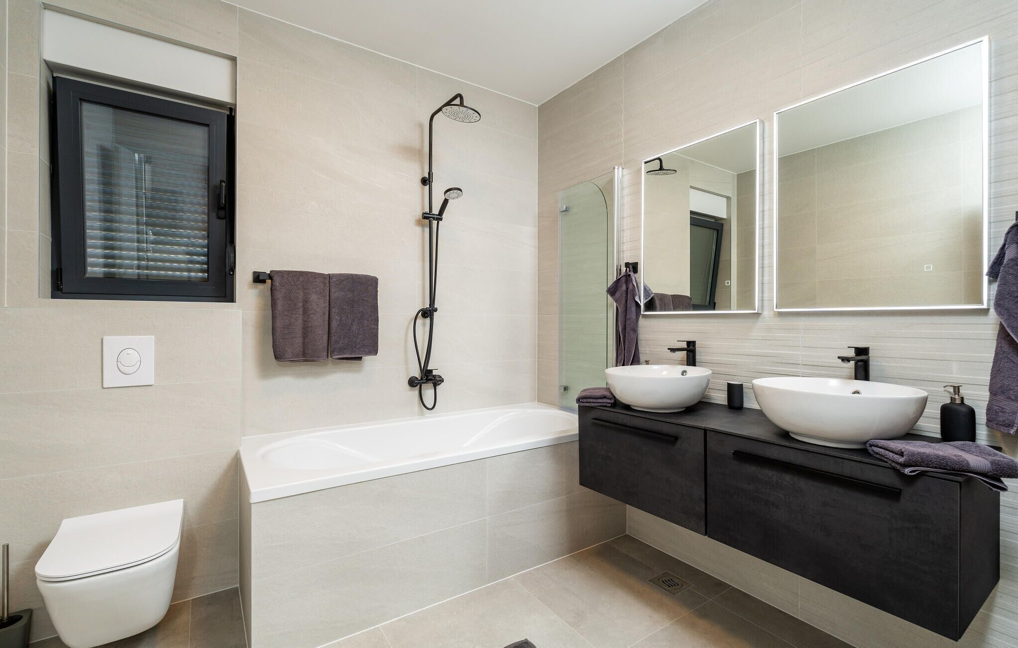 A modern bathroom with a bathtub, two sinks, a shower, and a toilet.