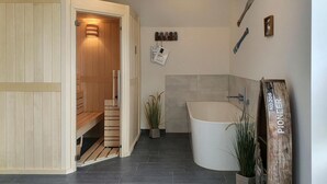 A modern bathroom with a freestanding bathtub, a wooden sauna, and a small potted plant. - Awesome home in Büsum with sauna (Büsum)