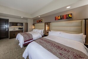Two single beds with white linens and patterned bedspreads, a kitchenette with microwave and coffee maker, and a flat-screen TV.
