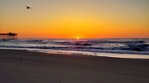 A beach with a pier extending into the ocean during sunset. - Dog Friendly, Kure Beach Cottage, 1/2 block walk; ready for your get-a-wave. (Kure Beach)