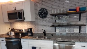 Una cocina moderna con armarios blancos, encimera de granito, microondas, cafetera y un reloj en la pared.