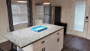 Una cocina con encimera de granito, armarios blancos, refrigerador de acero inoxidable y horno empotrado.