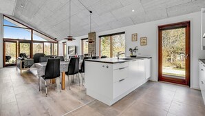 A modern kitchen with a central island, large windows, and a dining area with chairs and a table. - Nice home in Glesborg with sauna (Glesborg)