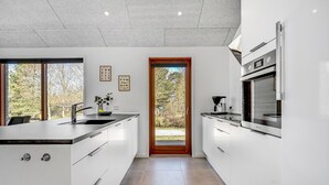 A modern kitchen with white cabinetry, a built-in oven, and a window overlooking a garden. - Nice home in Glesborg with sauna (Glesborg)