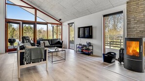A spacious living room with large windows, a fireplace, and a flat-screen TV. - Nice home in Glesborg with sauna (Glesborg)