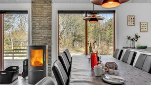 A modern dining area with a large table, chairs, a wood-burning stove, and a view of the outdoors. - Nice home in Glesborg with sauna (Glesborg)