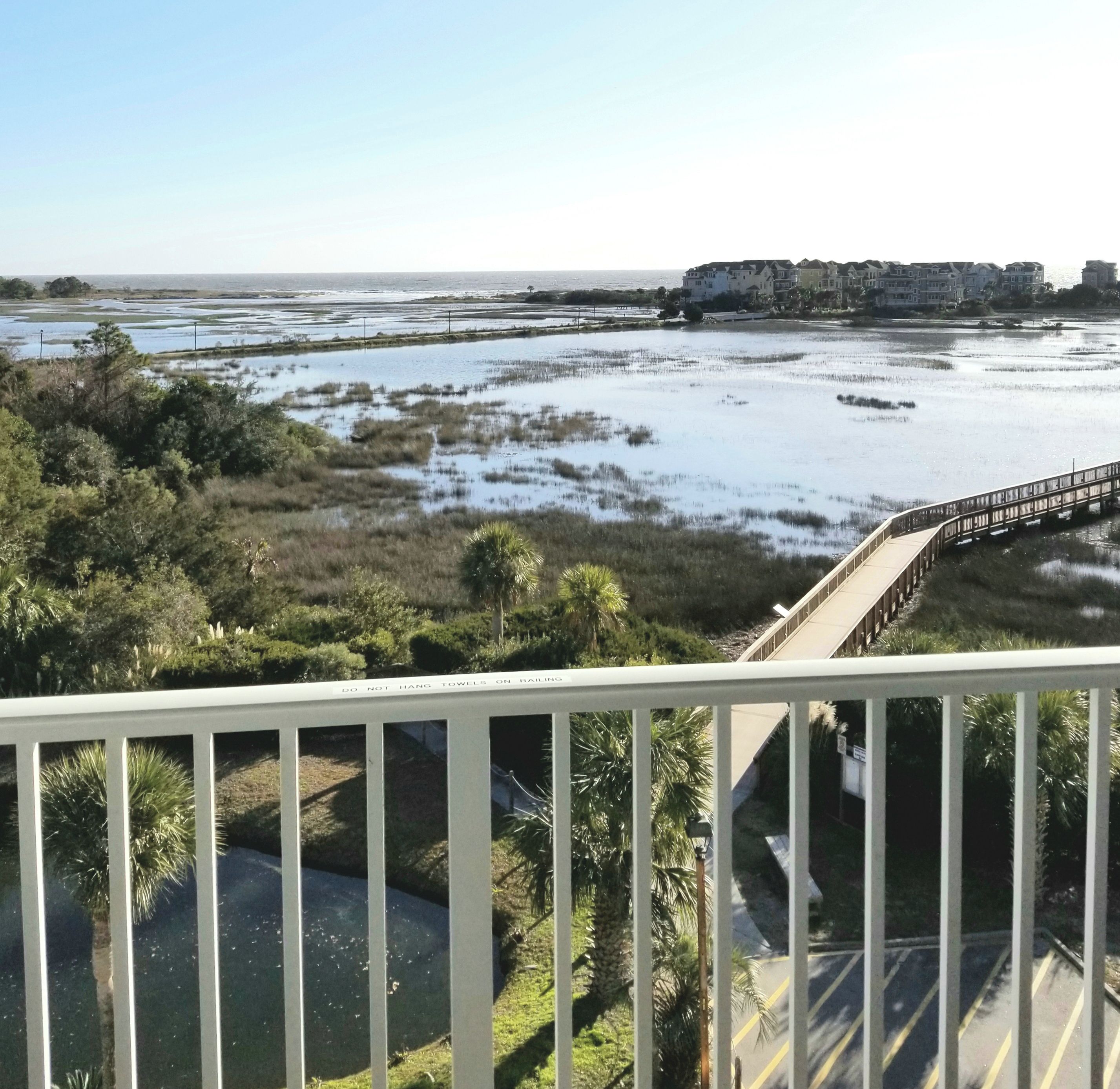 A view from a balcony overlooking a coastal area with a bridge, marshy land, and buildings in the distance.