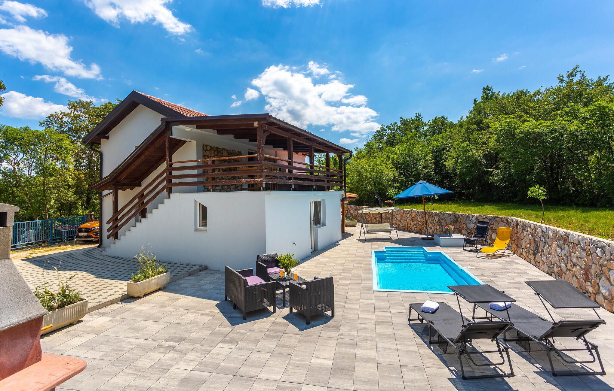 Ein zweistöckiges Haus mit Balkon, Schwimmbad, Gartenmöbeln und einer Steinmauer.