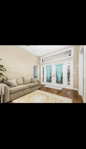 Un salon avec un canapé beige, un tapis à motifs et une grande fenêtre ornée de rideaux turquoise.