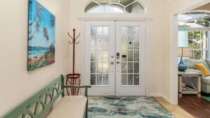 Ein Flur mit einer Bank, einer Tür mit satinierten Glasscheiben, einer Chandelierleuchtre und einem Gemälde mit Strandmotiv.