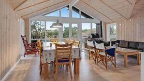 A spacious dining area with wooden tables and chairs, large windows offering views of the outdoors, and a modern kitchen with a grill. - 4 bedroom stunning home in Ribe (Ribe)