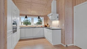 A modern kitchen with white cabinets, a wooden ceiling, and a window with a view of trees and a flag. - 4 bedroom stunning home in Ribe (Ribe)