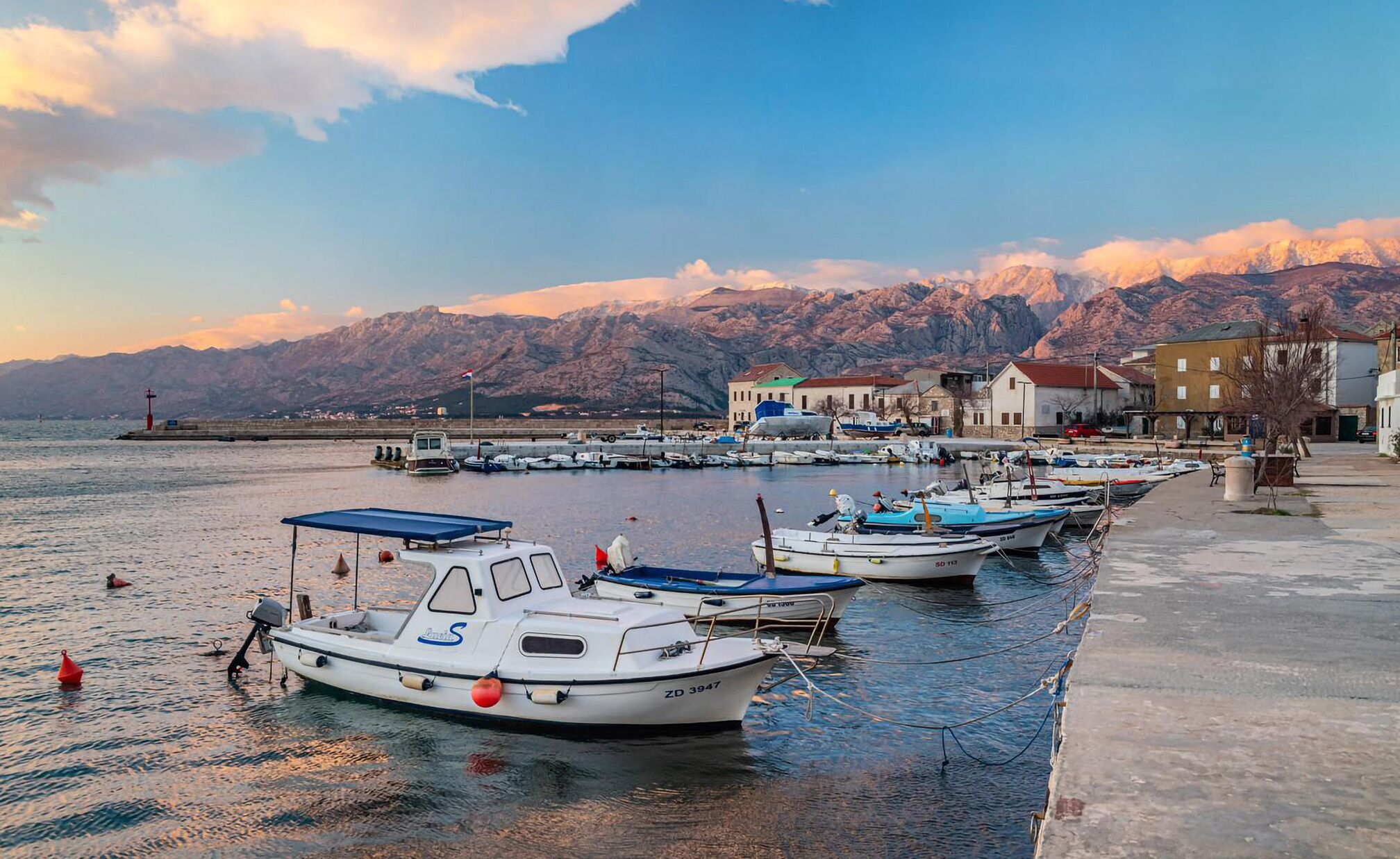 A marina with several boats docked, a pier, and a mountainous backdrop.