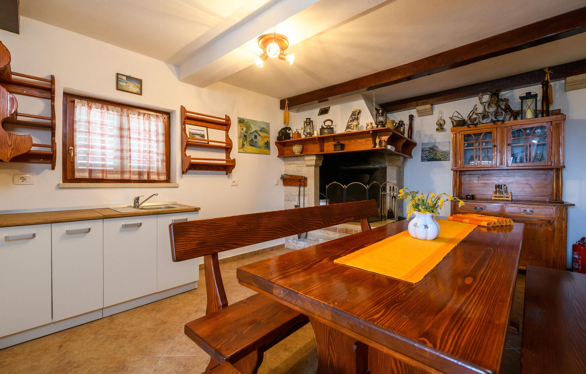 Une cuisine traditionnelle avec des meubles en bois, un banc intégré et une table à manger agrémentée d’un vase de fleurs.