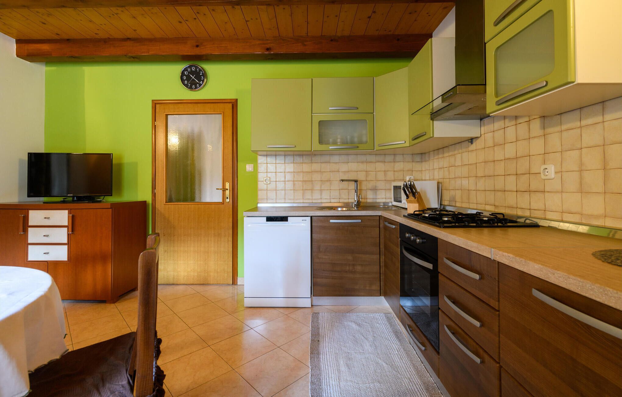 A compact kitchen with green cabinets, a white dishwasher, a stove, and a microwave.