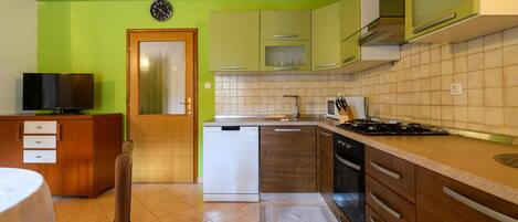 A compact kitchen with green cabinets, a white dishwasher, a stove, and a microwave.