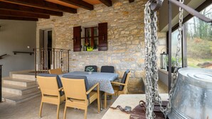 Eine Terrasse mit Steinwänden, Korbmöbeln, einem Metalltopf und einer Treppe, die zu einer erhöhten Ebene führt.