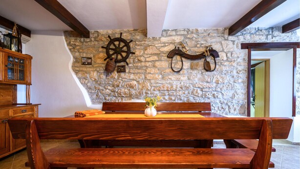 Ein rustikaler Essbereich mit einer Steinwand, einer hölzernen Bank und einem Tisch mit Blumen in einer Vase.