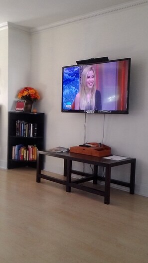 A television mounted on a wall with a bookshelf and a small table below it.