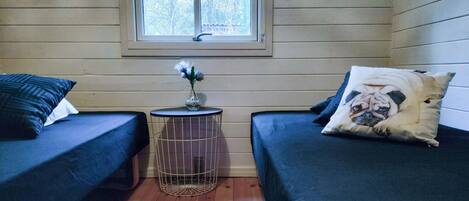 A room with two beds, a small round table with a vase of flowers, and a window with a view of trees.
