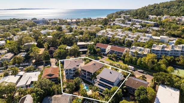 An aerial view of a coastal residential area with multiple buildings, a clear view of the sea, and a marked plot of land.