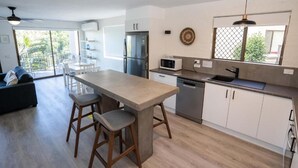 A modern kitchen with a central island, white cabinetry, stainless steel appliances, and a dining area with a sofa and chairs.