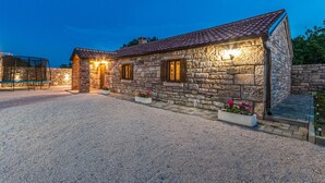 Un edificio in pietra con vialetto sterrato e zona relax coperta.