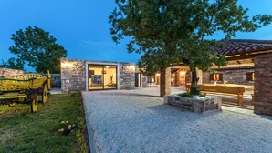 Un'area esterna moderna con un vialetto sterrato, una panchina in legno e un edificio in pietra con porte in vetro.