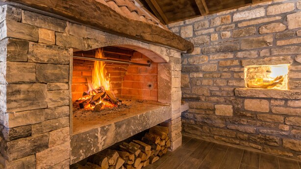 Un camino in pietra con un fuoco acceso all'interno, circondato da pareti in pietra e un soffitto in legno.