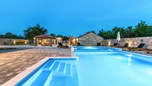 Una piscina con muro in pietra e lettini, un piccolo padiglione e un edificio in pietra con tetto a tegole.