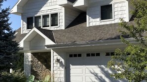 A two-story house with a garage, a stone foundation, and a clear blue sky.