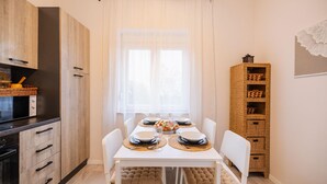 A modern kitchen with white cabinetry, a dining table set for four, and a wicker storage unit. - Lovely home in Seline (Seline)