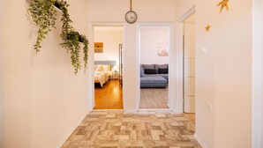 A hallway with a wooden parquet floor, a bed with white bedding, a grey sofa, and a wall-mounted clock. - Lovely home in Seline (Seline)