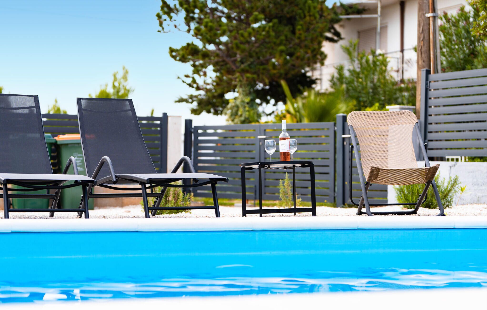 A poolside area with lounge chairs and a table with a bottle and glasses.