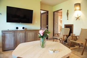 Un salon avec un téléviseur à écran plat, un meuble en bois, des fauteuils en osier, une table ronde et un vase rempli de fleurs.