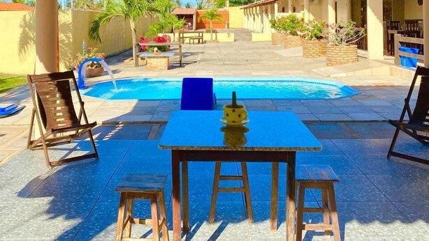 An outdoor pool area with a covered patio, a table with chairs, and a view of the surrounding landscape. - POUSADA SONHO DE MAR (Luis Correia)