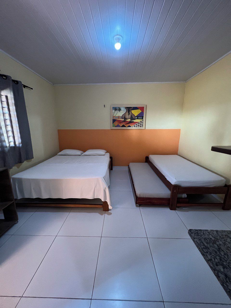 A room with two beds, a ceiling light, and a painting on the wall.