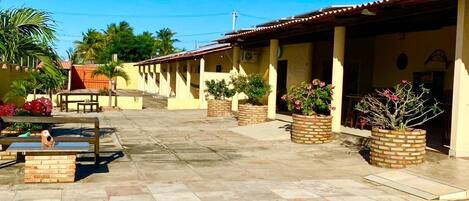 A pool area with a tiled deck, a swimming pool, and a covered patio with brick planters and outdoor furniture.