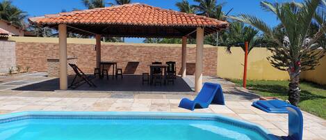 A swimming pool with lounge chairs and a covered seating area.